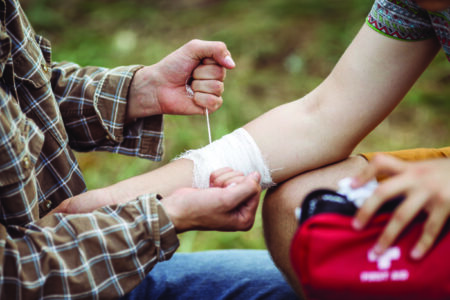 A person wrapping a second person's injured arm in gauze